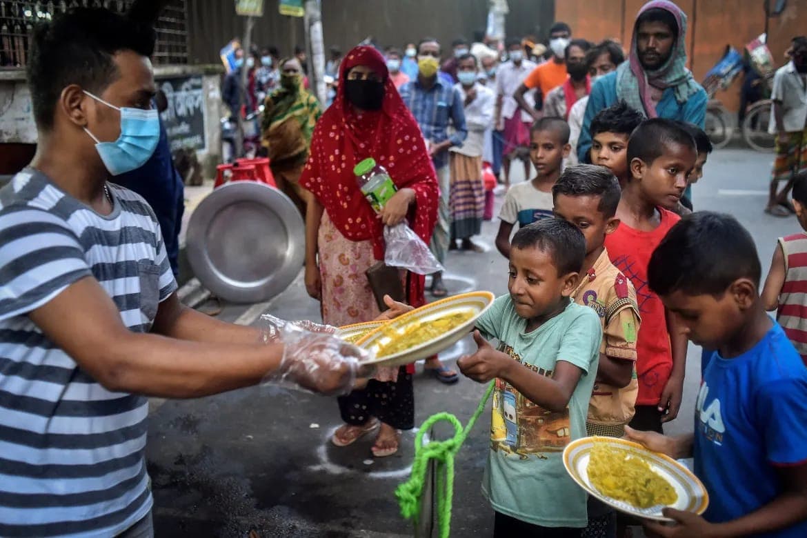 A volunteer handing plates of food to children waiting in line.